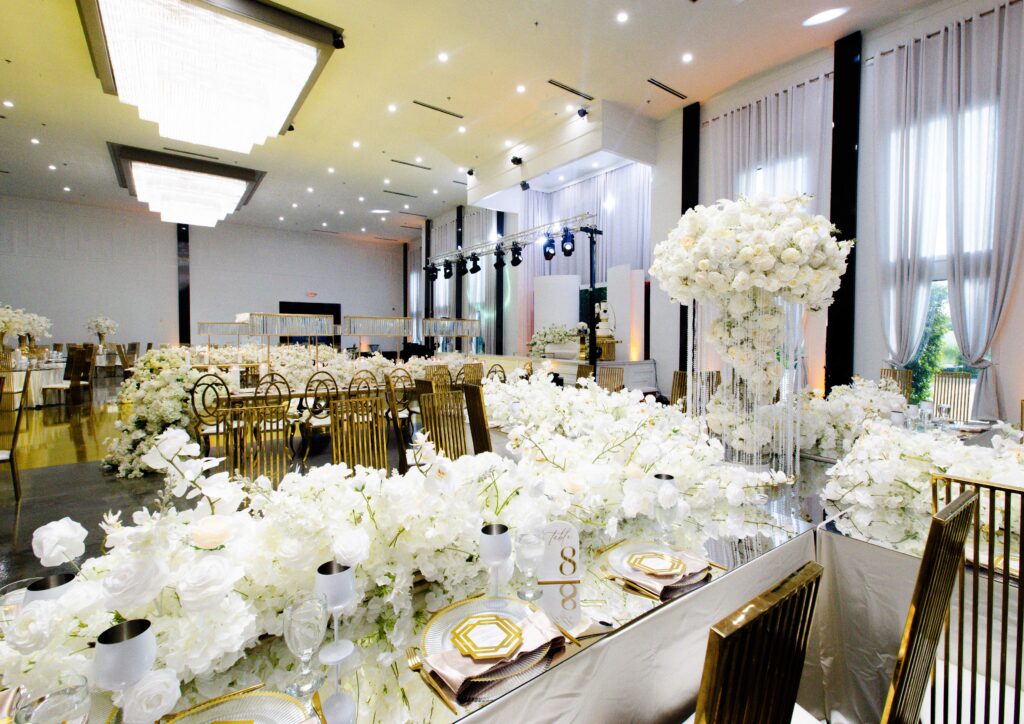 White floral luxury tablescape with layered arrangements, gold cutlery, water goblets, and mirrored table elements for an upscale wedding reception by Events D’Lux.