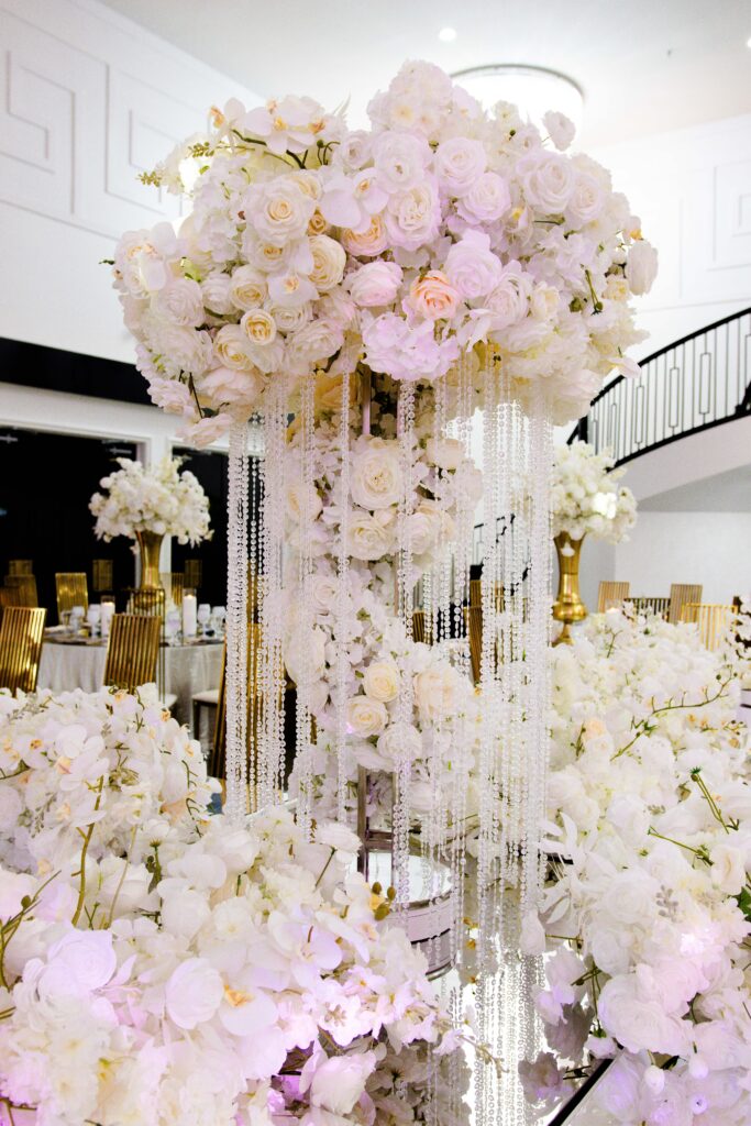Tall luxury wedding centerpiece with cascading crystal strands and lush white floral arrangement, designed by Events D’Lux for an elegant white-and-gold reception at The Hamptons Event Venue.