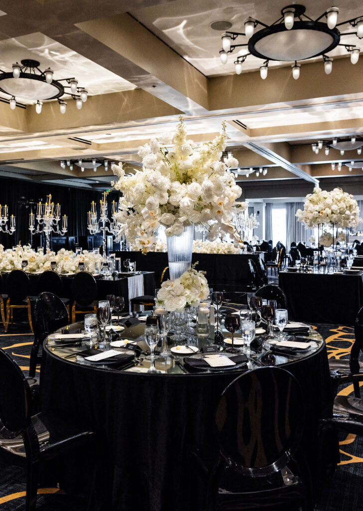 “Black satin luxury event tablescape with mirror top. layered linens and white floral arrangements.