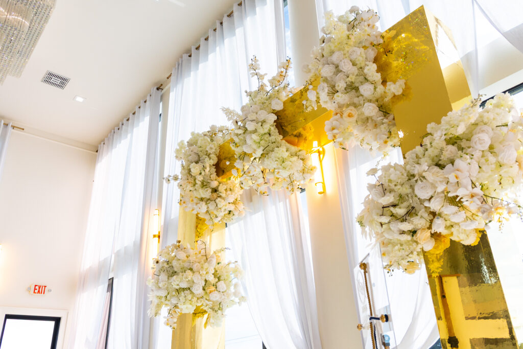 Side view of gold mirrored wedding arbor with tall white floral installations and natural light draping the chapel, part of a luxury ceremony design by Events D’Lux.