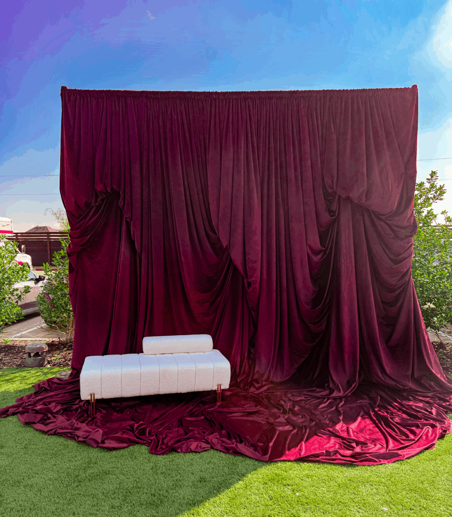 Deep burgundy velvet draping with layered folds and a modern white bench, showcasing heritage glamour and luxury event design.